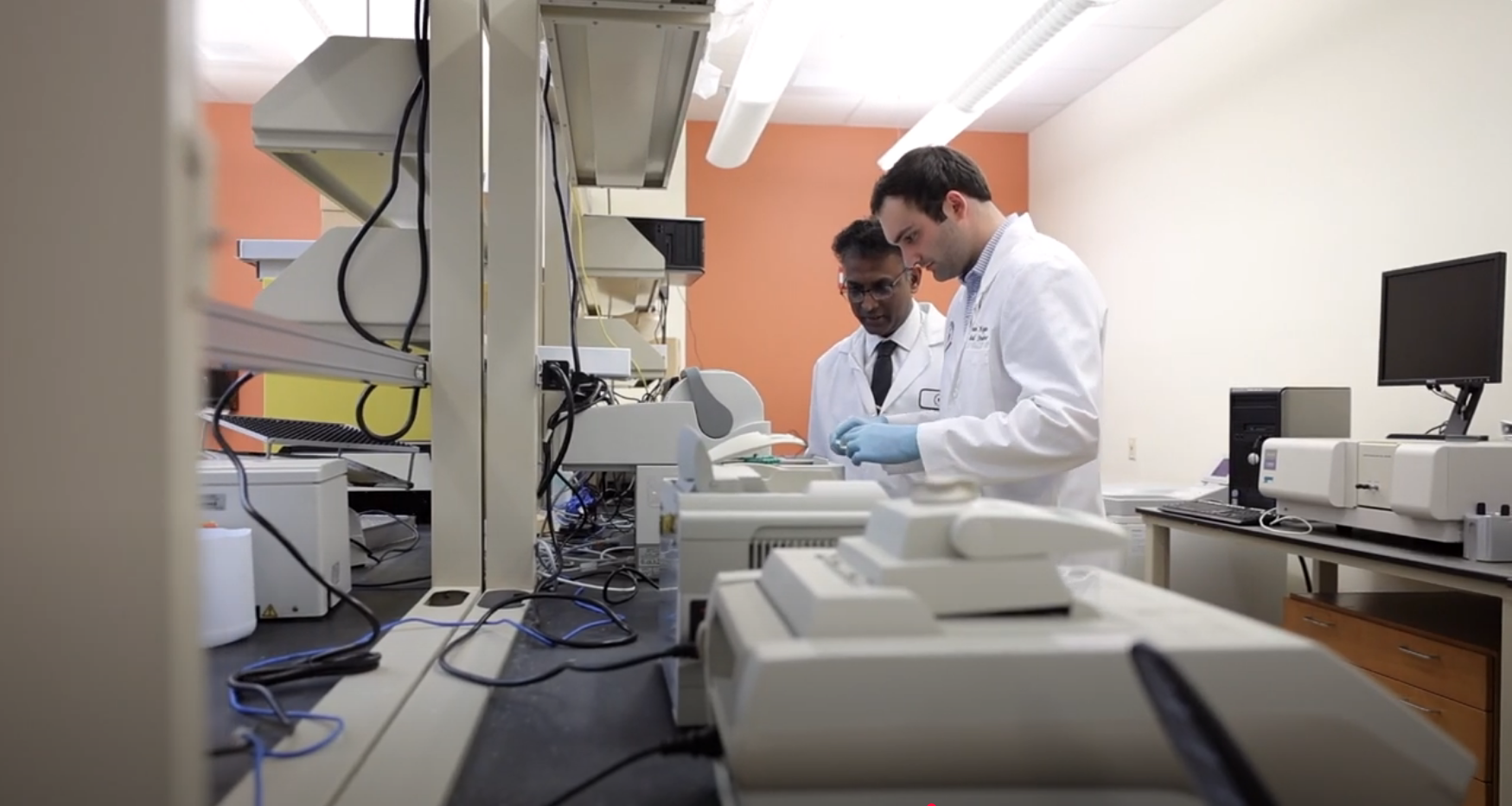 Professor and student in lab coats in research lab.